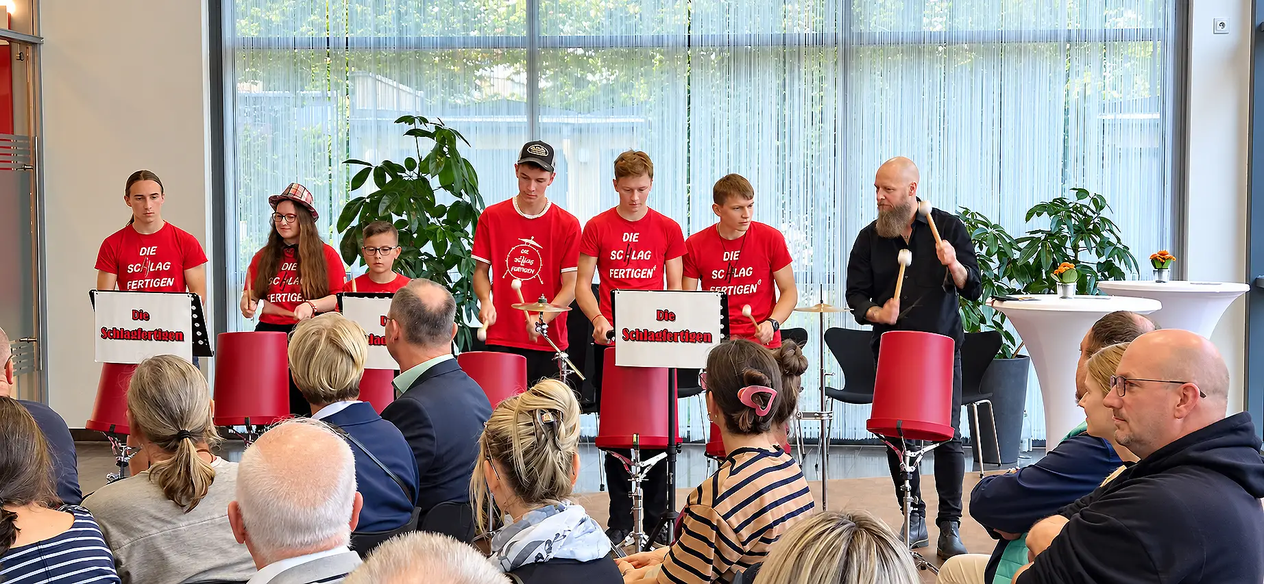 Schlagzeugensemble „Die Schlagfertigen“ bei einer Vernissage in einem Veranstaltungsraum; Publikum im Hintergrund.